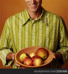 Portrait of a mature man holding a bowl of apples and smiling