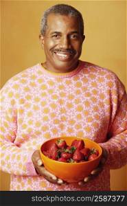 Portrait of a mature man holding a bowl of strawberries and smiling
