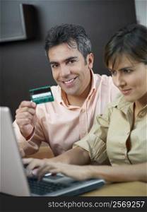 Portrait of a mature man holding a credit card and a mid adult woman using a laptop near him