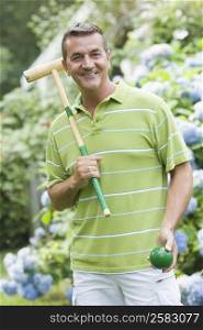 Portrait of a mature man holding a croquet mallet and a ball and smiling