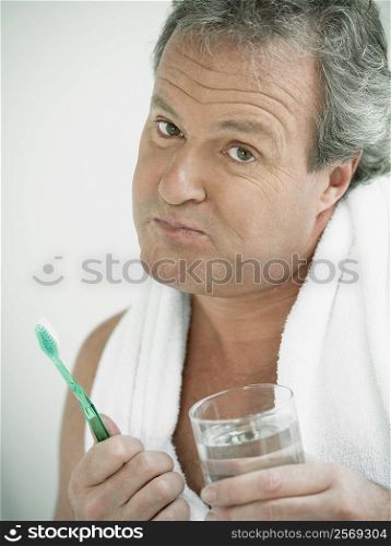 Portrait of a mature man holding a glass of water and a toothbrush