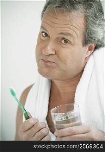 Portrait of a mature man holding a glass of water and a toothbrush