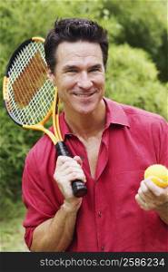Portrait of a mature man holding a tennis ball and a tennis racket