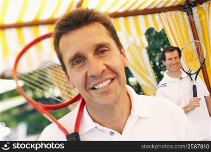 Portrait of a mature man holding a tennis racket and a mid adult man standing behind him