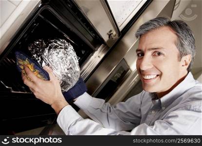 Portrait of a mature man inserting a dish wrapped in foil into a microwave and smiling
