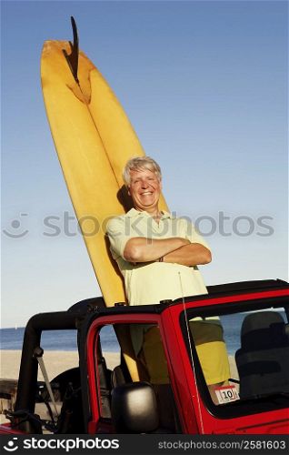 Portrait of a mature man leaning against a surfboard in a sports utility vehicle