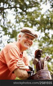 Portrait of a mature man leaning on a golf bag and smiling
