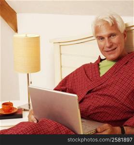 Portrait of a mature man leaning on the bed with a laptop