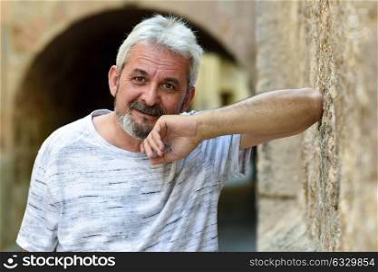 Portrait of a mature man looking at camera in urban background. Senior male with white hair and beard smiling wearing casual clothes.