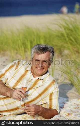 Portrait of a mature man lying on the beach and holding a champagne flute