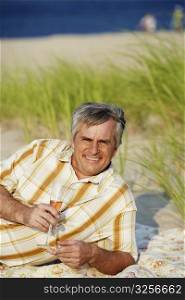 Portrait of a mature man lying on the beach and holding a champagne flute