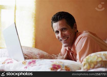 Portrait of a mature man lying on the bed with a laptop and smiling