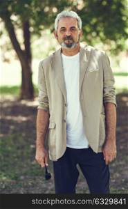 Portrait of a mature man, model of fashion, in an urban park. Senior male with white hair and beard wearing casual clothes.