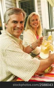 Portrait of a mature man pouring lemon juice in a glass with a mature woman sitting beside her