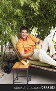 Portrait of a mature man reclining on a lounge chair and holding a glass of juice