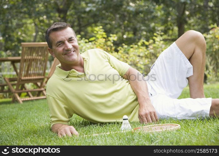 Portrait of a mature man reclining on grass with a badminton racket and a shuttlecock