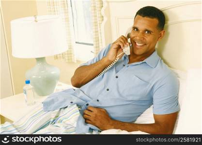 Portrait of a mature man reclining on the bed and talking on the telephone