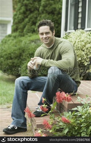 Portrait of a mature man sitting at doorsteps and holding a cup of coffee