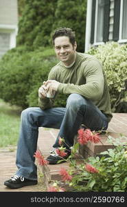 Portrait of a mature man sitting at doorsteps and holding a cup of coffee