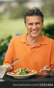 Portrait of a mature man sitting at the table with a plate of vegetable salad in front of him