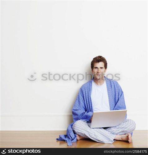 Portrait of a mature man sitting cross-legged on the floor and using a laptop