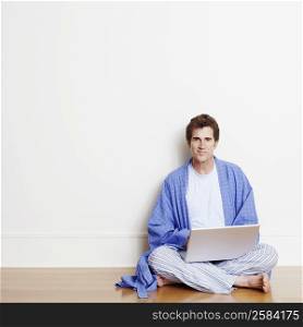 Portrait of a mature man sitting cross-legged on the floor and using a laptop