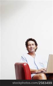 Portrait of a mature man sitting in an armchair and using a laptop