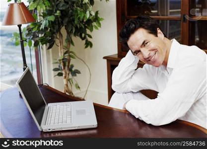 Portrait of a mature man sitting in front of a laptop and smiling
