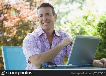 Portrait of a mature man sitting in front of a laptop and smiling