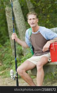 Portrait of a mature man sitting on a bench and holding a fishing rod