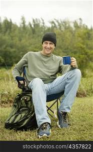 Portrait of a mature man sitting on a folding chair holding a mug