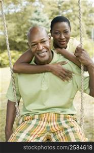 Portrait of a mature man sitting on a rope swing with a mid adult woman embracing him