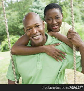 Portrait of a mature man sitting on a rope swing with a mid adult woman embracing him