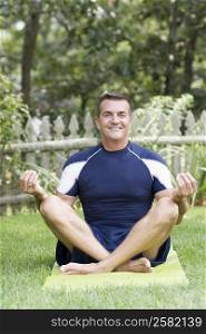 Portrait of a mature man sitting on an exercise mat in lotus position and smiling