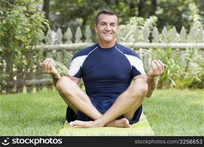 Portrait of a mature man sitting on an exercise mat in lotus position and smiling