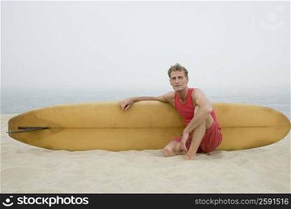 Portrait of a mature man sitting on the beach and holding a surfboard