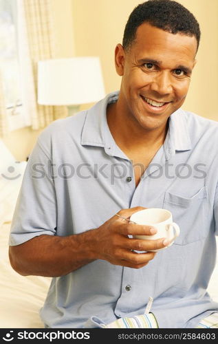 Portrait of a mature man sitting on the bed and holding a cup of tea