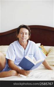Portrait of a mature man sitting on the bed holding a book