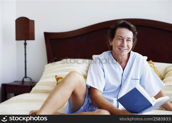 Portrait of a mature man sitting on the bed with a book and smiling