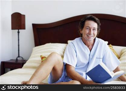 Portrait of a mature man sitting on the bed with a book and smiling
