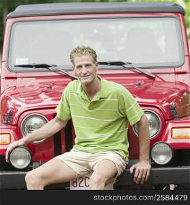 Portrait of a mature man sitting on the bumper of a jeep and smiling