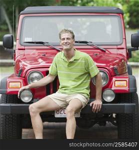 Portrait of a mature man sitting on the bumper of a jeep and smiling