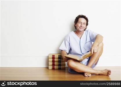 Portrait of a mature man sitting on the floor with a book and smiling
