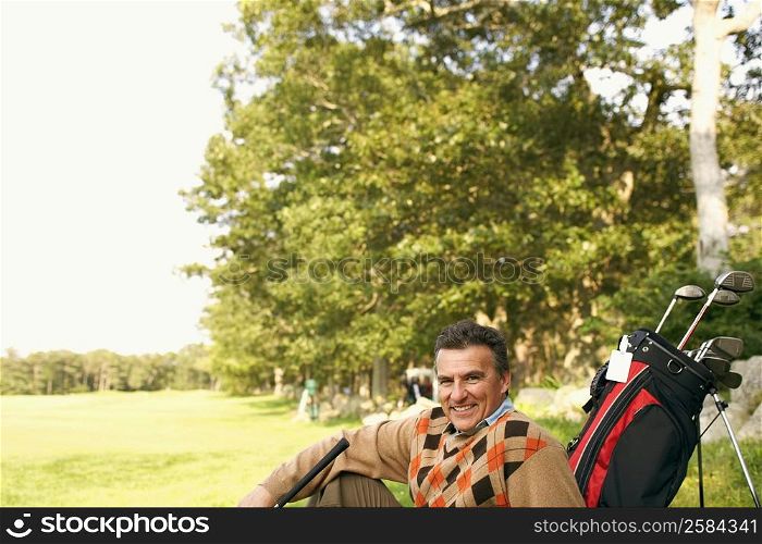 Portrait of a mature man sitting with a golf bag on a golf course