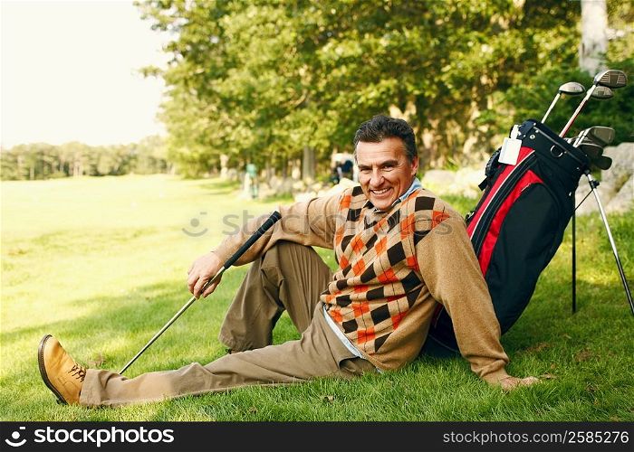 Portrait of a mature man sitting with a golf bag on a golf course