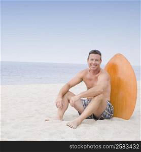 Portrait of a mature man sitting with a surfboard on the beach and smiling