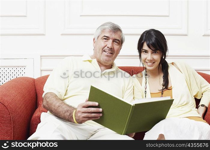 Portrait of a mature man sitting with his daughter on a couch and holding a book