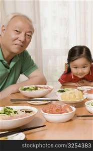 Portrait of a mature man sitting with his granddaughter at a dining table