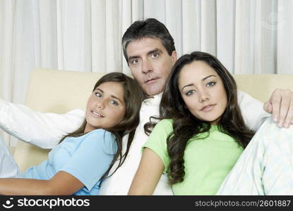 Portrait of a mature man sitting with his two daughters on a couch