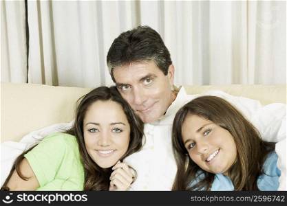 Portrait of a mature man sitting with his two daughters on a couch and smiling